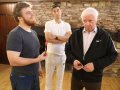 FI0A8021-Giuseppe-Tom-and-Derek-Giuseppe-hold-dart-Tom-arms-folder-Derek-defeated-cropped